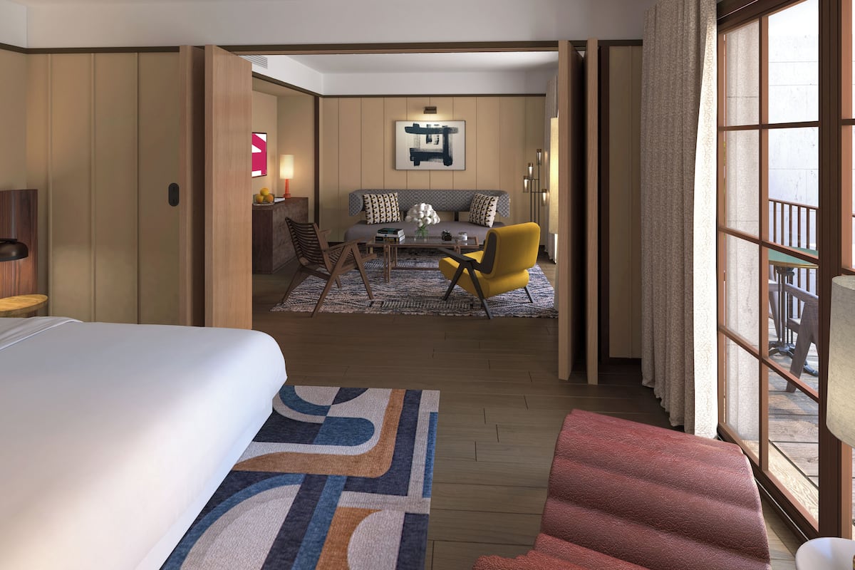 Habitación de hotel con una cama grande, una zona de estar con sofá y sillas, una mesa de comedor y vistas a través de un ventanal.