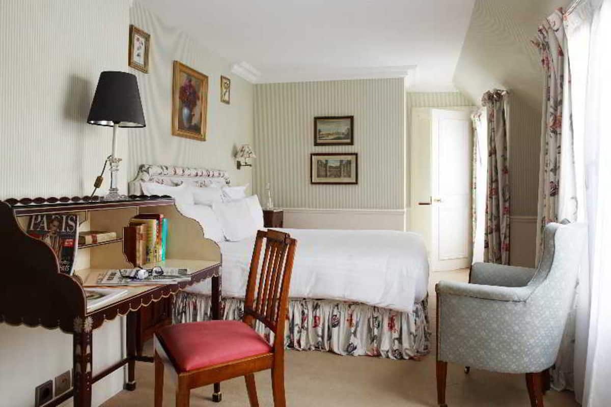 Una habitación de hotel con una cama, un escritorio con lámpara, una silla y una estantería.