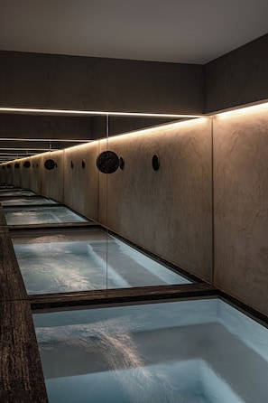 A row of individual shower stalls with a reflective floor, each stall separated by a wall with circular cutouts. - Norman Hôtel & spa - Paris Champs-elysées (Paris)