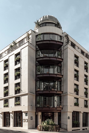 Un hotel de varios pisos con una cúpula central, balcones con plantas y un diseño arquitectónico clásico.