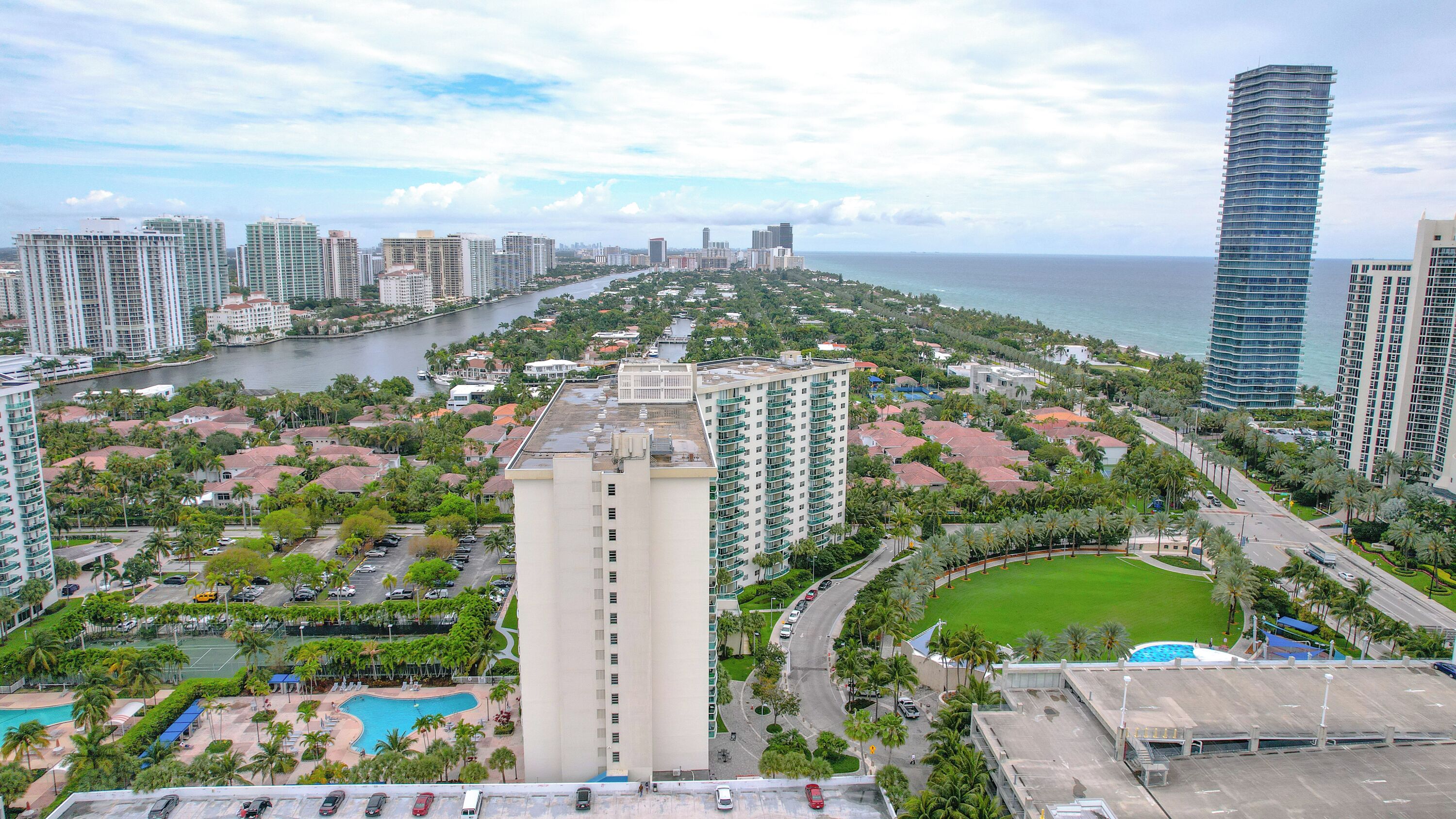 A high-rise hotel with a swimming pool, a tennis court, and a view of the city and ocean.