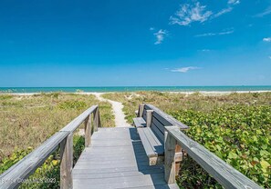 A wooden boardwalk leading to a beach with a clear view of the ocean.