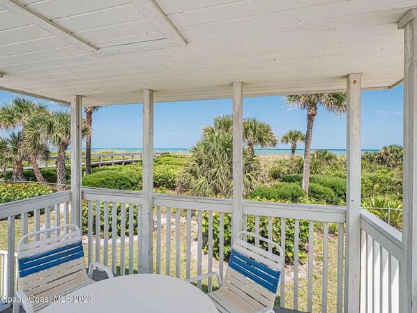 A covered outdoor area with a white railing, a table, and two chairs.