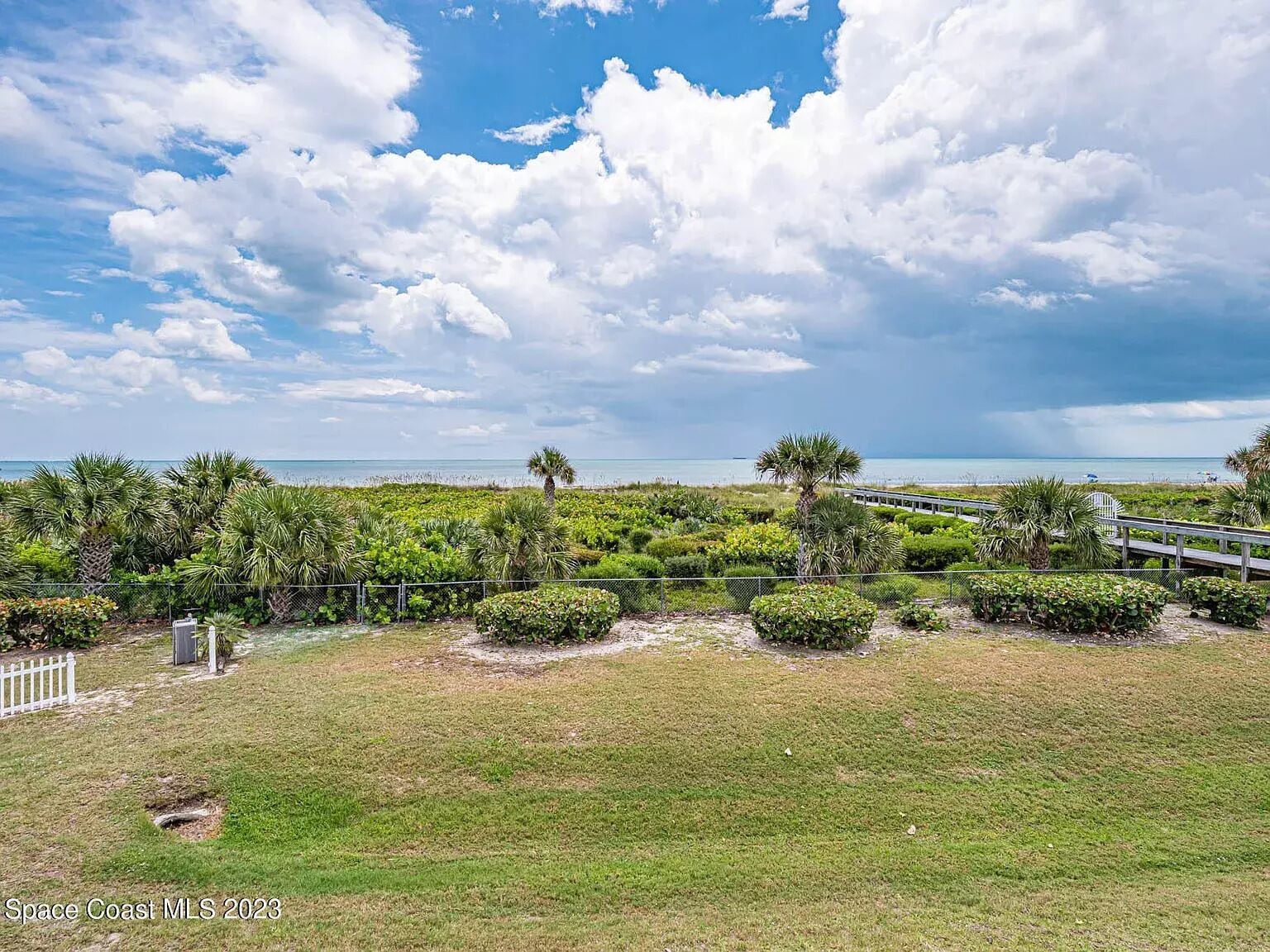 Un paisaje costero con una zona cubierta de hierba, un paseo marítimo de madera y vista al océano.