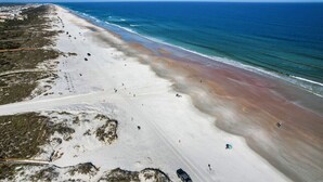 A beach with a long stretch of sand, a few people, and a clear blue sky.