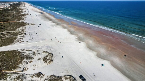Een strand met een lange zandvlakte, enkele mensen en een helderblauwe lucht.