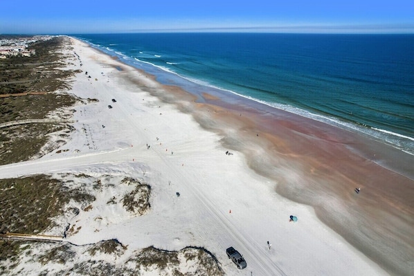 Una playa con una extensa franja de arena, algunas personas y un cielo azul despejado.