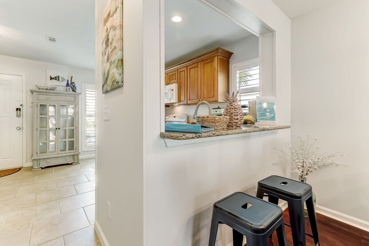 A kitchen with wooden cabinets, a microwave, and a countertop with decorative items. There are two stools and a vase with branches.