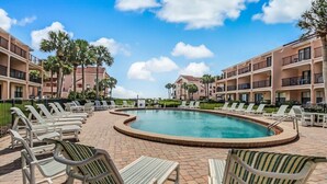 A pool area with lounge chairs and a swimming pool, surrounded by multi-story buildings with balconies.