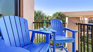 Een balkon met twee blauwe Adirondack-stoelen en een kleine tafel, een waterfles en een glas.