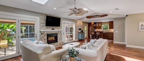 A spacious living room with a fireplace, a ceiling fan, and a large TV.