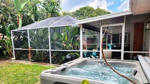 Una vasca idromassaggio con struttura in vetro, immersa nel verde e circondata da un patio coperto.