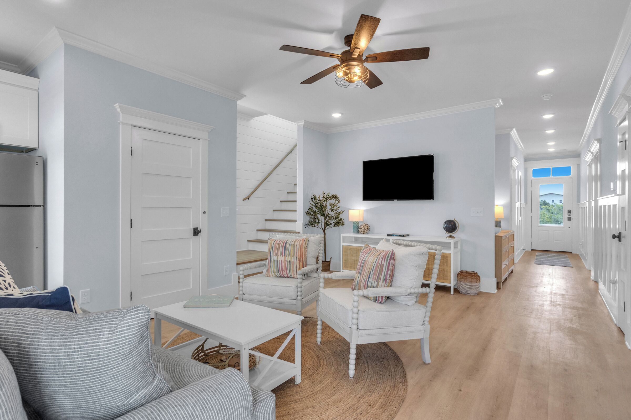 A modern living room with a staircase, a flat-screen TV, and a ceiling fan.