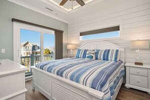 A bedroom with a bed, bedside tables, a window, and a view of houses outside. - Slow M'Ocean: Large, Modern Home with a Pool, Elevator and Hot Tub! (Oak Island)