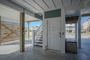 A covered entrance with a wooden fence, a white door, and a staircase leading to a residential area. - Slow M'Ocean: Large, Modern Home with a Pool, Elevator and Hot Tub! (Oak Island)