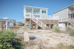 A beachfront property with a multi-level wooden deck, a staircase leading to the upper floor, and a sandy beach area. - Slow M'Ocean: Large, Modern Home with a Pool, Elevator and Hot Tub! (Oak Island)