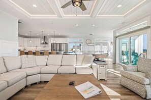 A modern living room with a sectional sofa, a wooden coffee table, and a view of the kitchen and dining area. - Slow M'Ocean: Large, Modern Home with a Pool, Elevator and Hot Tub! (Oak Island)