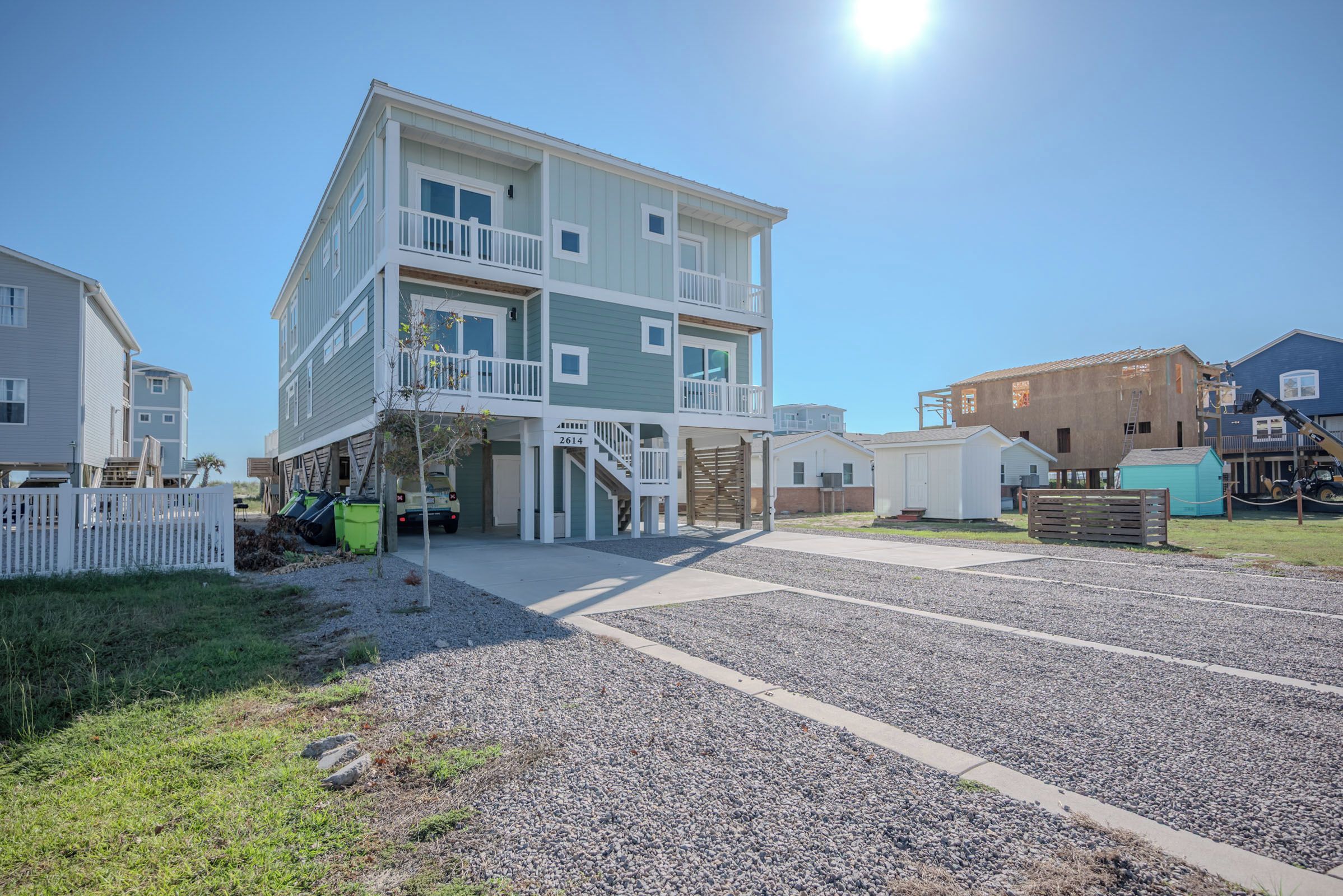 A multi-story residential building with a balcony on the second floor, a covered entryway, and a gravel driveway.