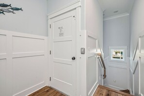 A hallway with white walls, a wooden floor, and a door with a vent. - Slow M'Ocean: Large, Modern Home with a Pool, Elevator and Hot Tub! (Oak Island)
