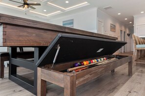 Une table de billard dotée d’un compartiment de rangement intégré, contenant des billes et des queues de billard.