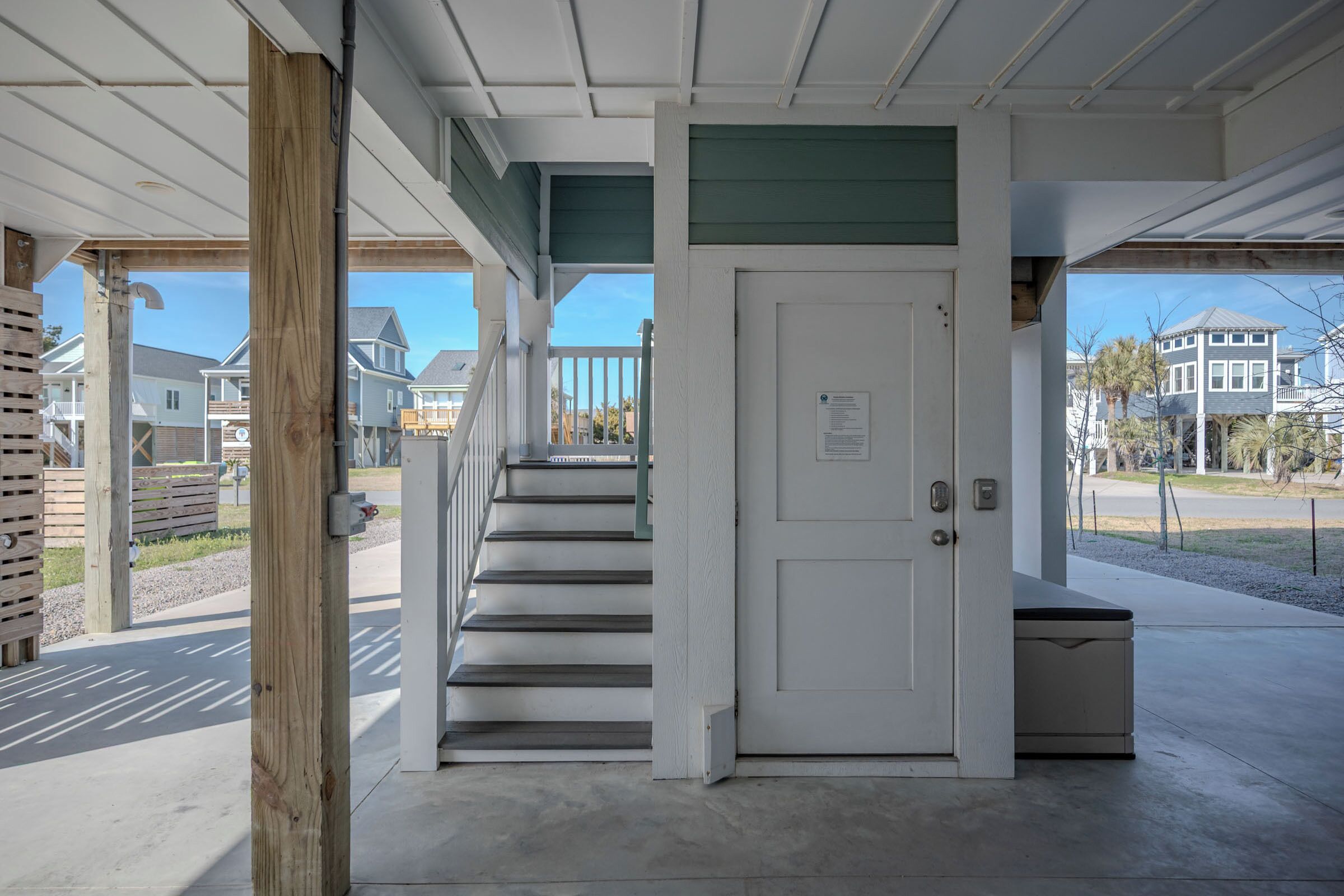A covered outdoor staircase leading to a white door, with a view of residential houses in the background.