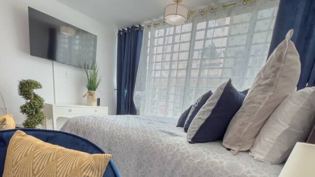 A modern bedroom with a bed, a blue sofa, a bedside table with a lamp, and a TV mounted on the wall. - Seaside Studio on Isla Verde Beach (Carolina)