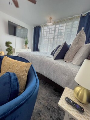 A modern bedroom with a bed, a blue sofa, a bedside table with a lamp, and a TV mounted on the wall. - Seaside Studio on Isla Verde Beach (Carolina)