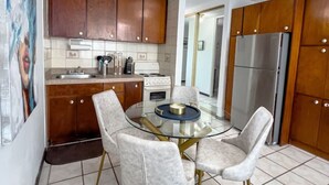 A modern kitchen with wooden cabinets, a stainless steel refrigerator, and a glass dining table with four chairs. - Seaside Studio on Isla Verde Beach (Carolina)