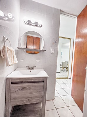 Bathroom features a sink, vanity with drawer, and round mirror.