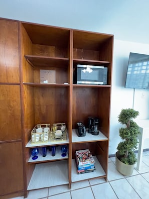 Cozy living space features a shelving unit with a microwave, books, and a potted plant, alongside a mounted TV.