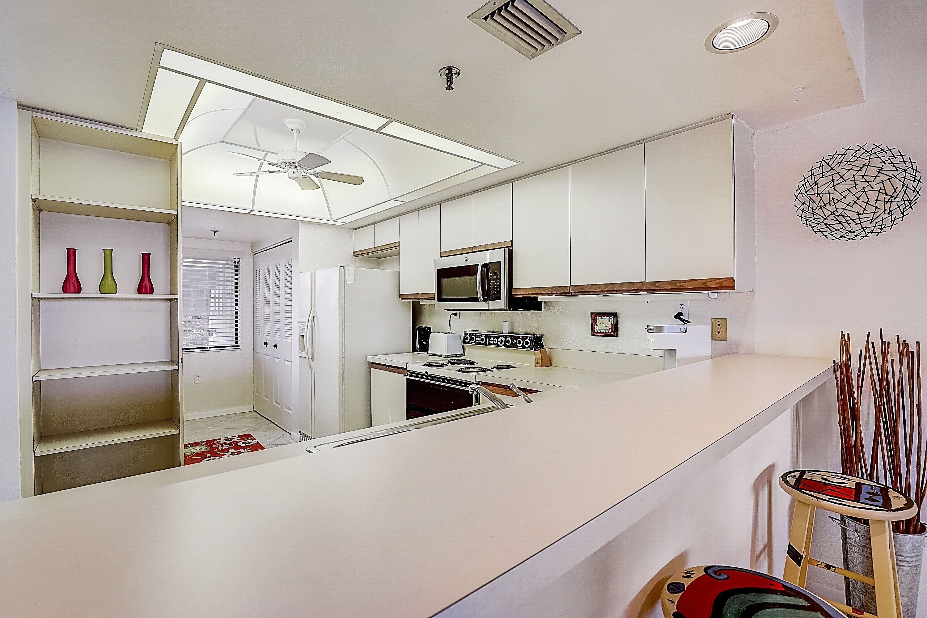 Una cocina moderna con armarios blancos, un microondas y un ventilador de techo.