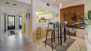 A modern kitchen with white cabinets, a microwave, and a dining area with stools and a table.