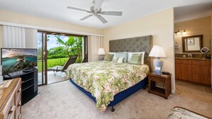 A bedroom with a large bed, a ceiling fan, a TV, a desk, and a view of the outdoors.