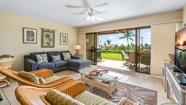 A spacious living room with a sofa, wicker chairs, a glass coffee table, and a television.