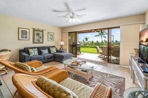 A spacious living room with a sofa, wicker chairs, a glass coffee table, and a television. - Big Island Keauhou Punahele A103 2 Bedroom Condo (Kailua-Kona)