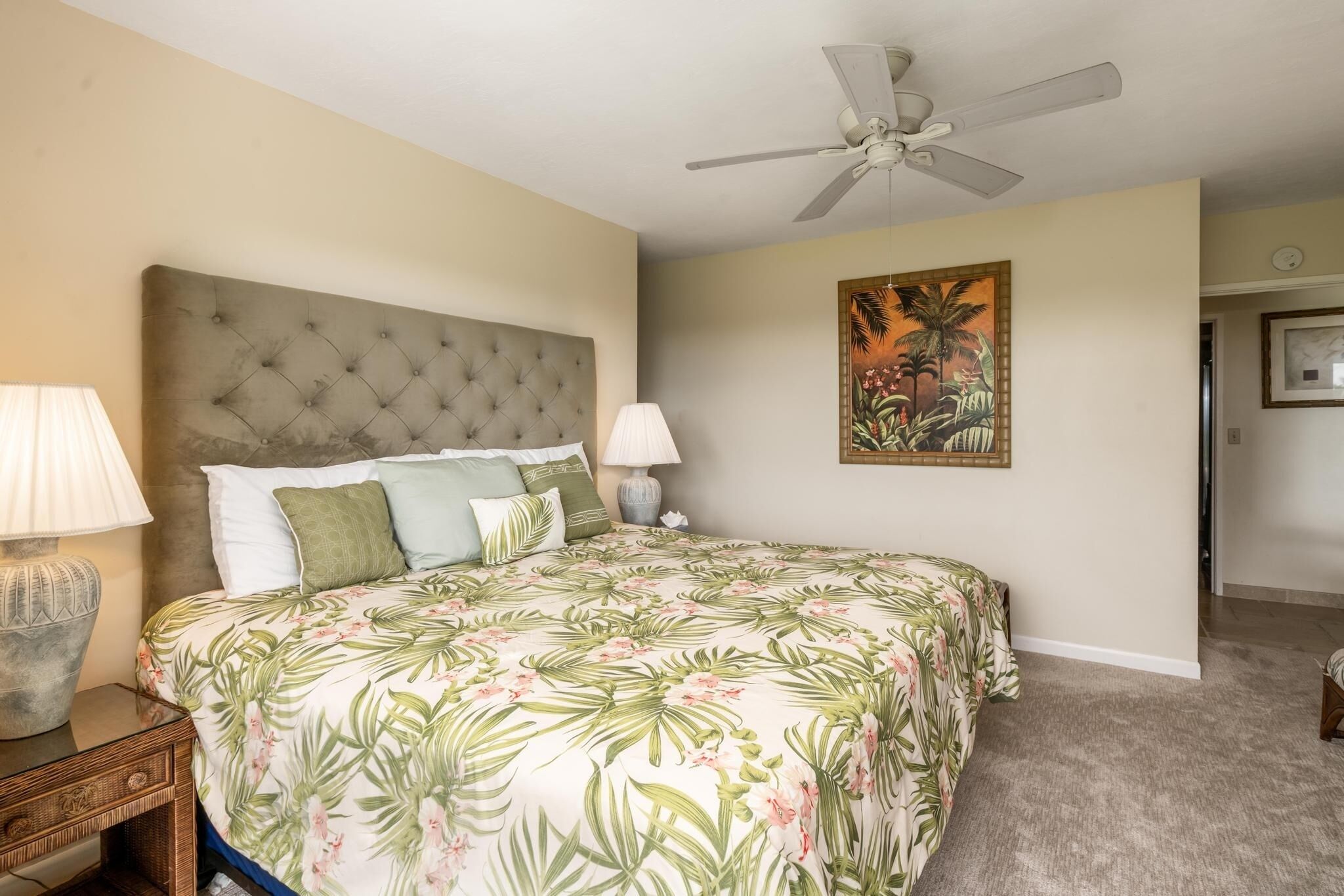 A bedroom with a tufted headboard, floral bedspread, two bedside lamps, and a ceiling fan.