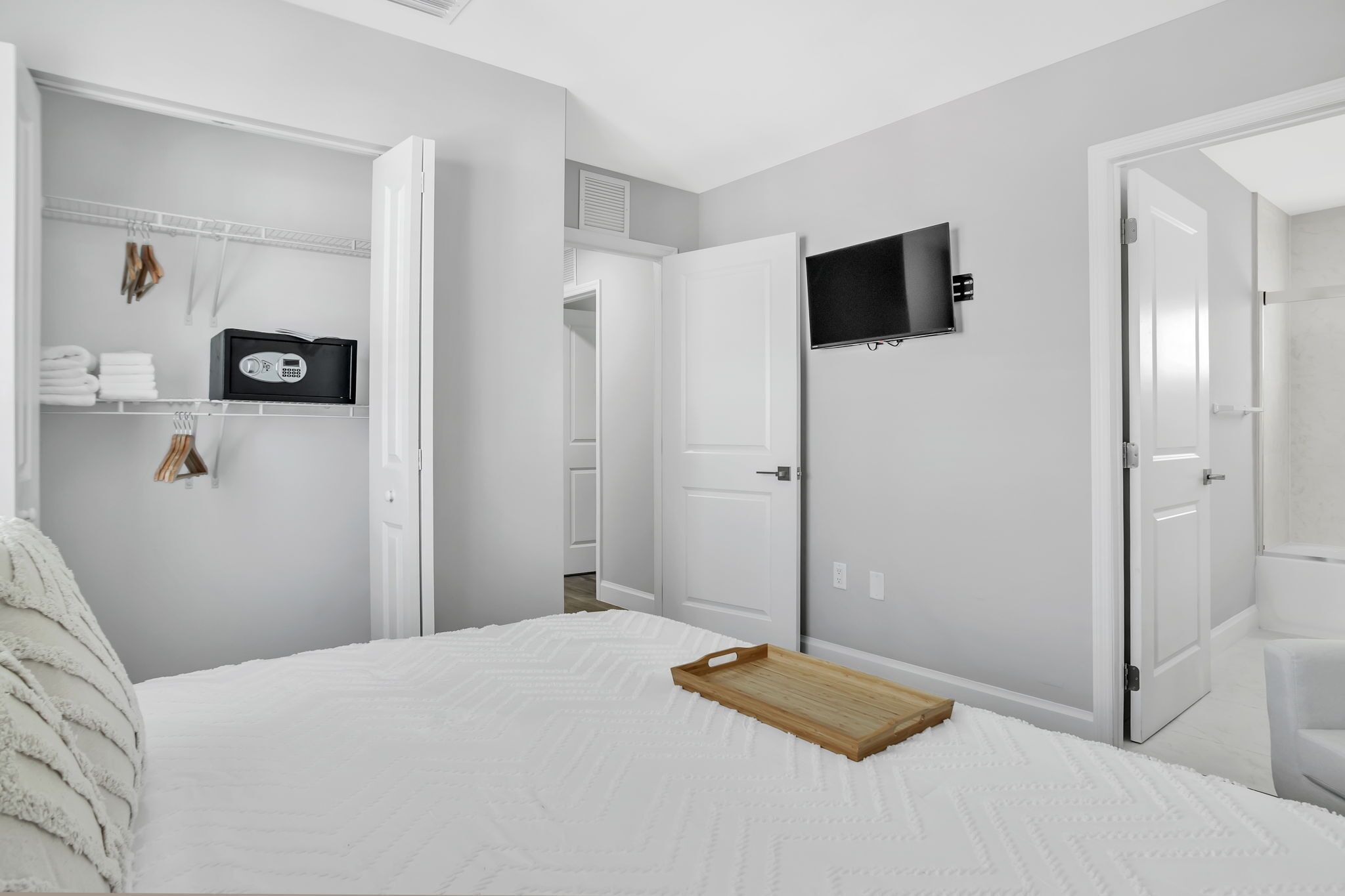 A bedroom with a bed, a TV mounted on the wall, and a closet with hanging clothes.