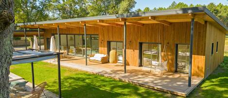 Eine moderne Holzdiele mit überdachter Terrasse, Glasüren und Gartenmöbeln.