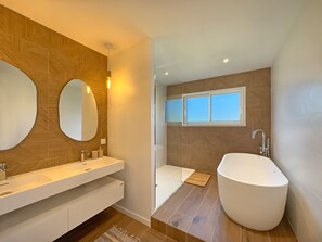 Een moderne badkamer met een vrijstaand bad, een grote spiegel en een wastafelmeubel met wastafel.