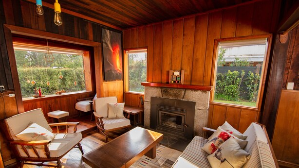 A cozy room with wooden walls, a fireplace, a sofa, a coffee table, and two chairs.