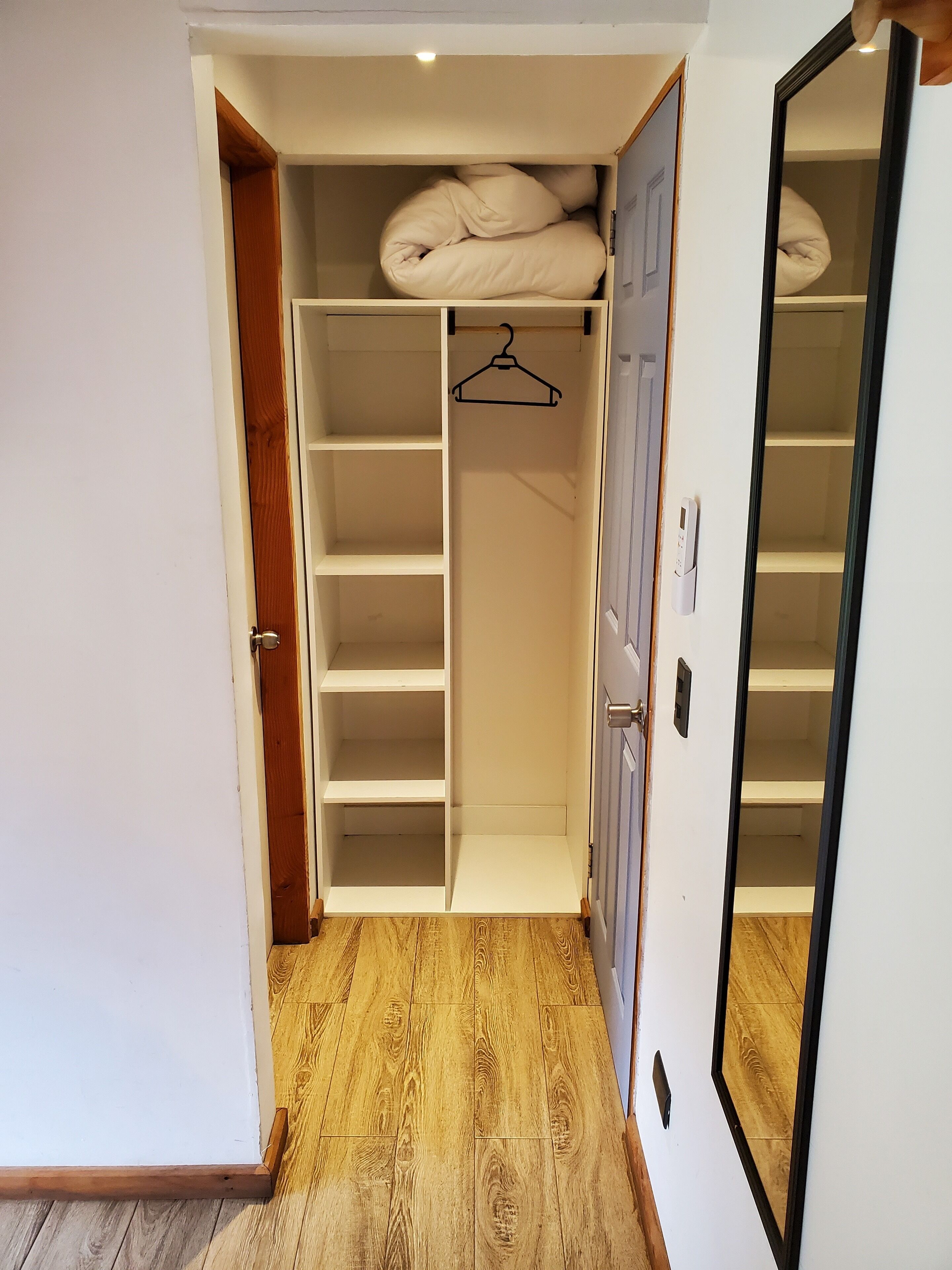 Un vestidor amplio con varios estantes y espacio para colgar ropa, suelo de madera y un espejo.