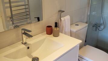 Un baño moderno con un lavamanos blanco, una cabina de ducha con paredes de vidrio y un inodoro.