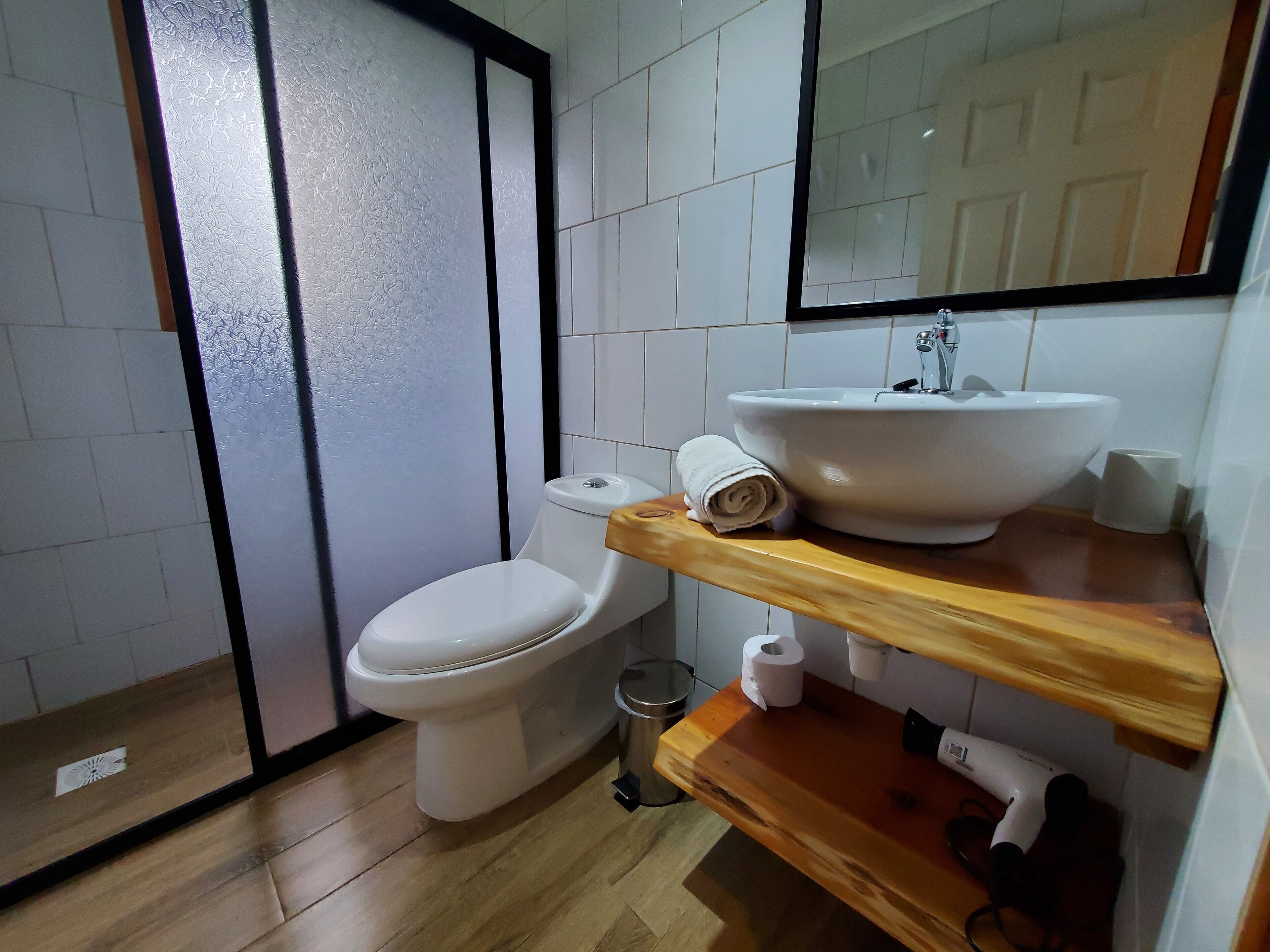 A bathroom with a toilet, a sink, a mirror, and a wooden shelf.