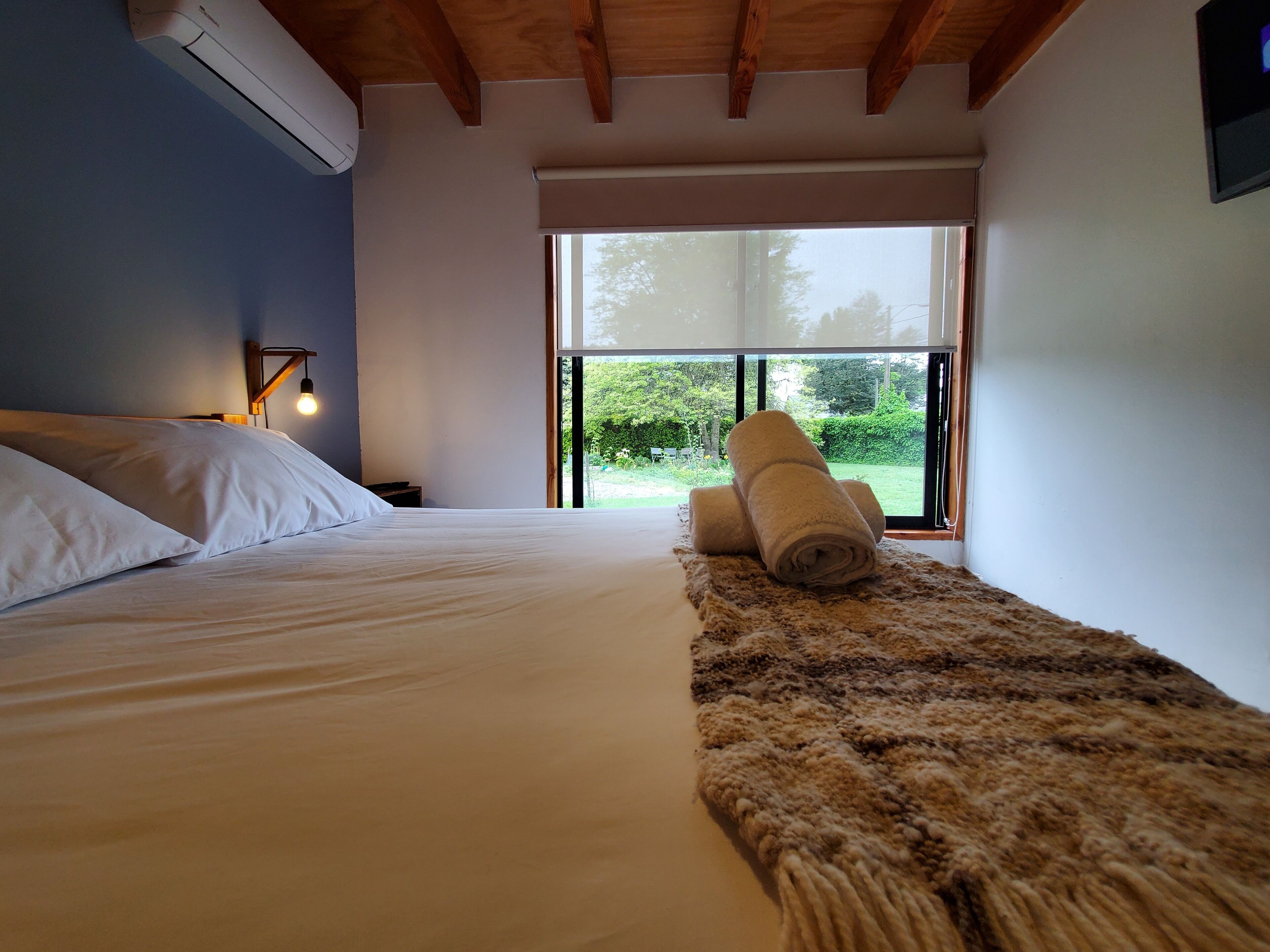 A bedroom with a bed, a window, and a rolled-up towel on a rug.