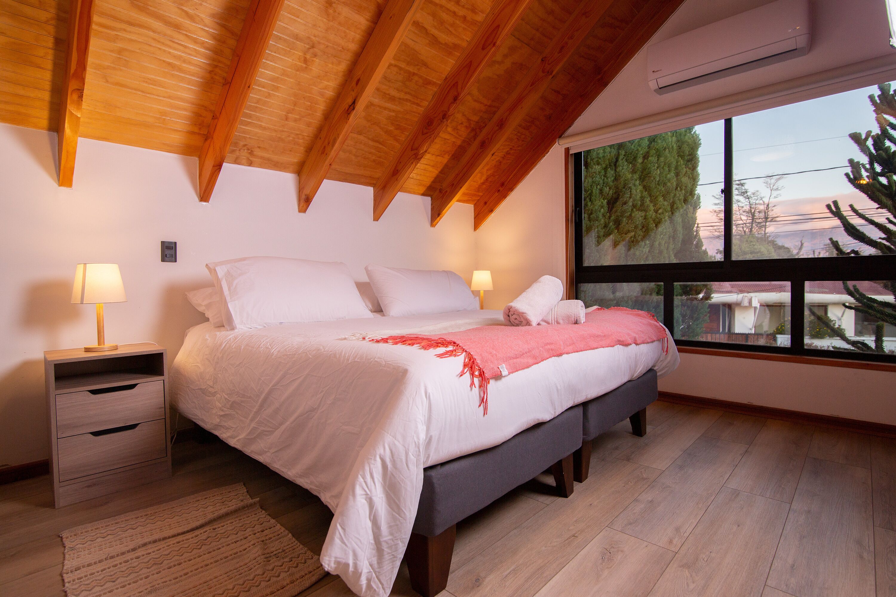 A bedroom with a bed, bedside tables, a window, and a wooden ceiling.