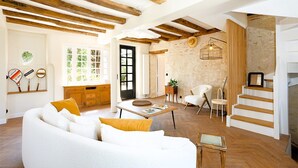 A spacious living room with a white sofa, wooden beams, a dining area, and a staircase. - La maison Berry (Vouvray)