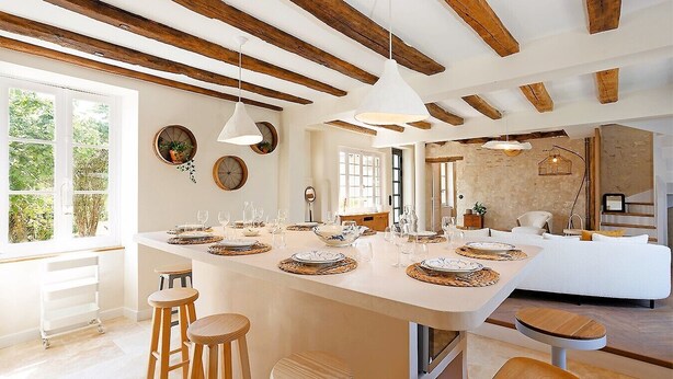 A spacious kitchen with a large island, wooden beams, and a view of the outdoors. - La maison Berry (Vouvray)