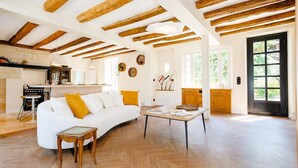 A spacious living area with a white sofa, wooden beams, and a kitchen in the background. - La maison Berry (Vouvray)