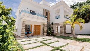 A modern two-story house with a balcony, a wooden door, and a small patio area. - Villa Belle Mar with a pool and within walking distance of the beach!  (Puerto Plata)
