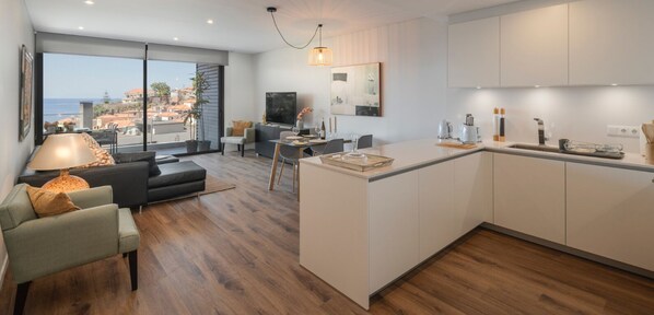 Une cuisine moderne avec un îlot central, un coin repas avec une table et des chaises, et un salon avec un canapé et une lampe.
